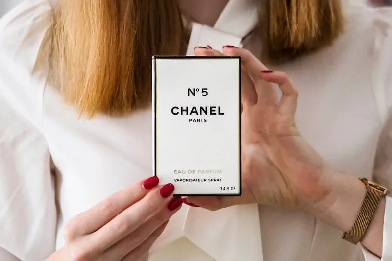 Deux mains tiennent une boîte de parfum, avec la mention « Eau de Parfum » et le volume affichés sur la face avant