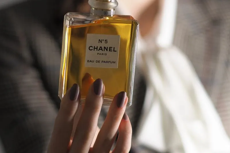 Main tenant un flacon de parfum dont l'étiquette affiche clairement la mention « Eau de Parfum »