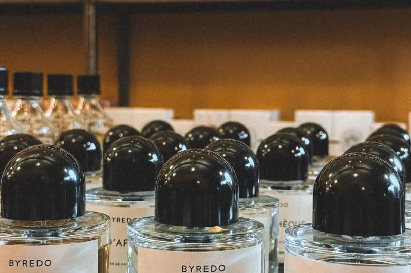Rangées de flacons de parfum de la même marque, tous de même forme à bouchon noir arrondi, alignés sur un présentoir de boutique