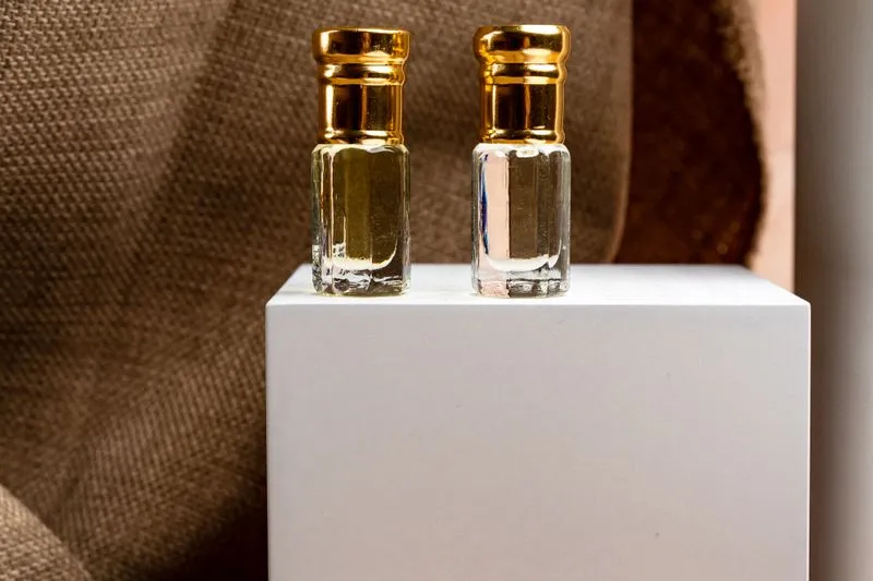 Deux flacons miniatures de parfum à bouchon doré, posés sur un socle blanc