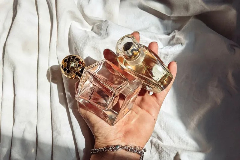 Une main tient deux flacons de parfum différents, l'un devant l'autre, à la lumière du jour