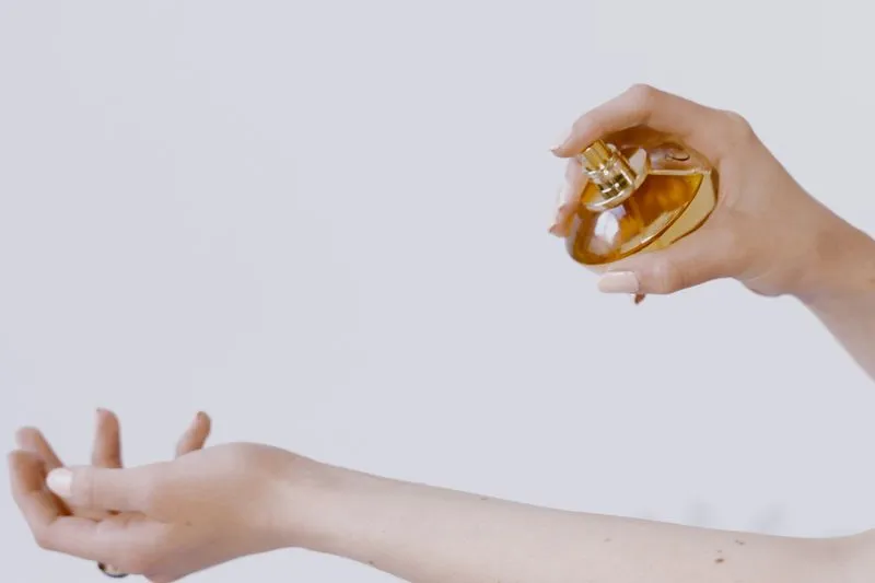 Femme qui vaporise du parfum au-dessus de l'intérieur de son avant-bras, le flacon tenu à bonne distance de la peau