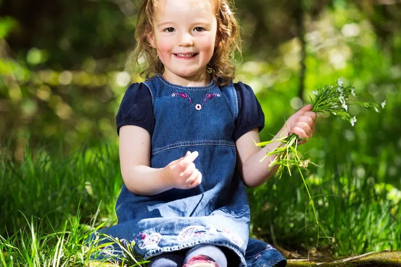 Petite fille assise dans l'herbe, un bouquet de fleurs sauvages à la main