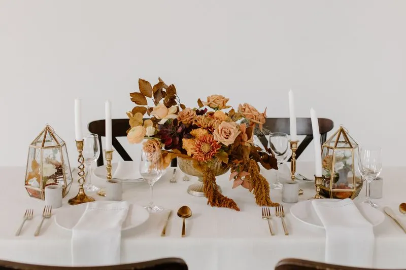 Table dressée avec bougies hautes, verres à pied et un bouquet aux tons cuivrés