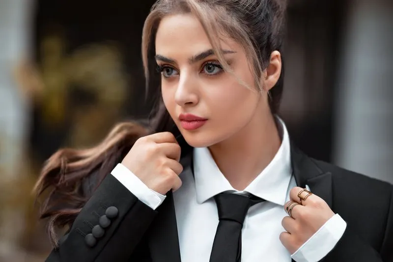 Portrait d'une femme en veste noire, chemise blanche et cravate, la main sur le col