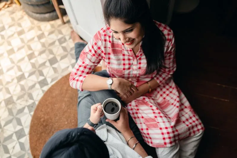 Jeune femme souriante appuyée contre son compagnon qui tient une tasse, moment complice à la maison