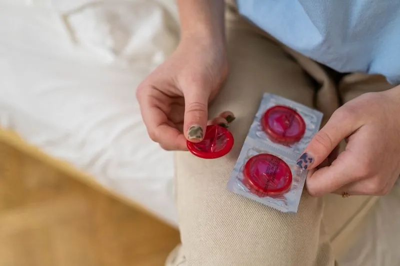 Mains tenant un préservatif déballé à côté d'un sachet encore scellé