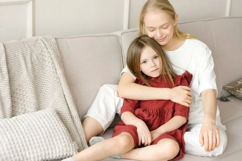 Mère et fille assises sur un canapé, la mère enlaçant tendrement sa fille