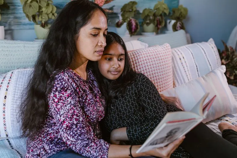 Une mère et sa fille d'une dizaine d'années, blotties l'une contre l'autre sur un canapé, lisent un livre ensemble