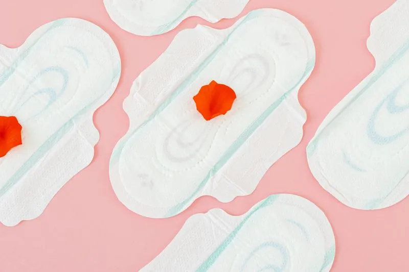 Plusieurs serviettes hygiéniques disposées sur un fond rose, certaines ornées d'un pétale rouge
