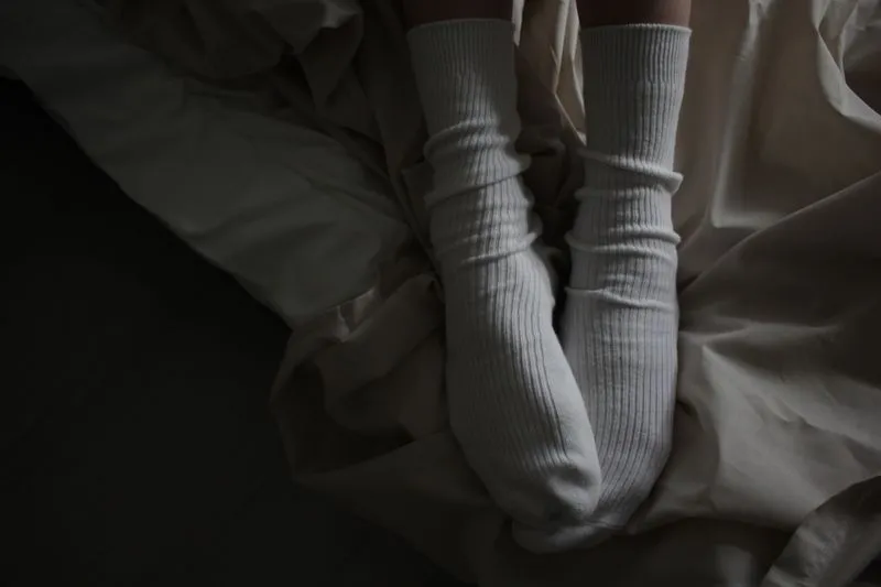 Pieds en chaussettes de coton blanches posés sur une couette claire