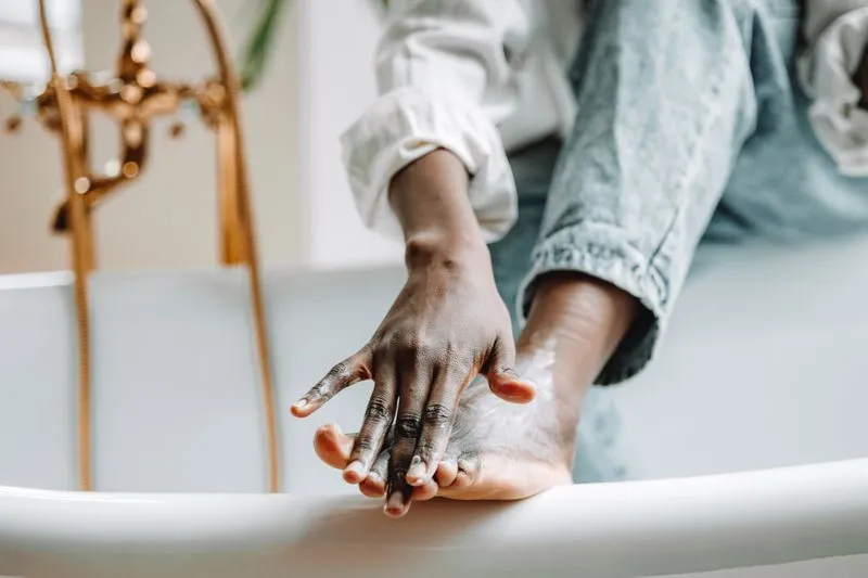 Main enduisant de crème le talon d'un pied posé sur le rebord d'une baignoire
