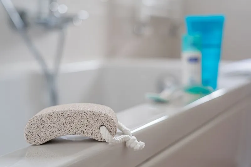 Pierre ponce grise posée sur le rebord d'une baignoire, à côté de produits de soin pour la peau