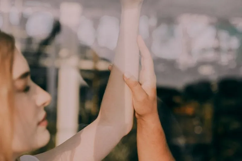 Une main qui touche l'intérieur de l'avant-bras levé d'une femme, dans une lumière dorée