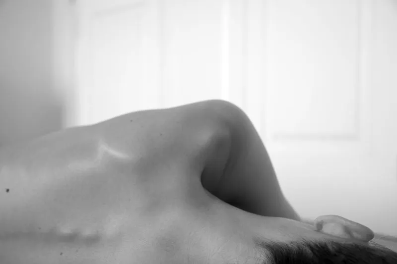 Gros plan en noir et blanc sur l'épaule et le haut du dos nus d'une femme allongée