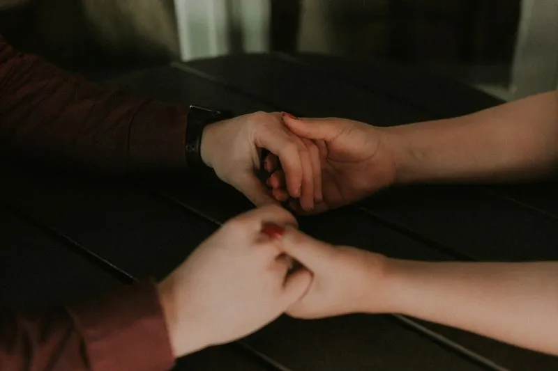 Deux personnes qui se tiennent les mains au-dessus d'une table sombre, dans la pénombre