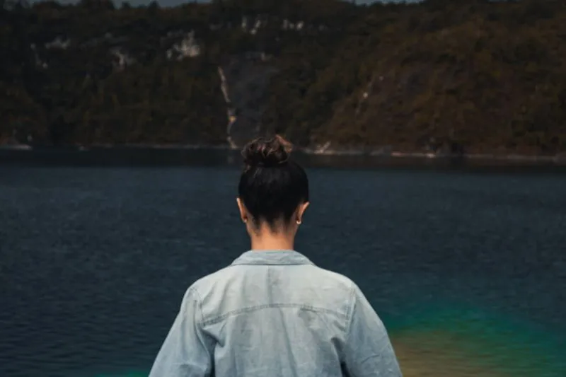 Nuque d'une femme aux cheveux relevés en chignon, vue de dos face à un lac
