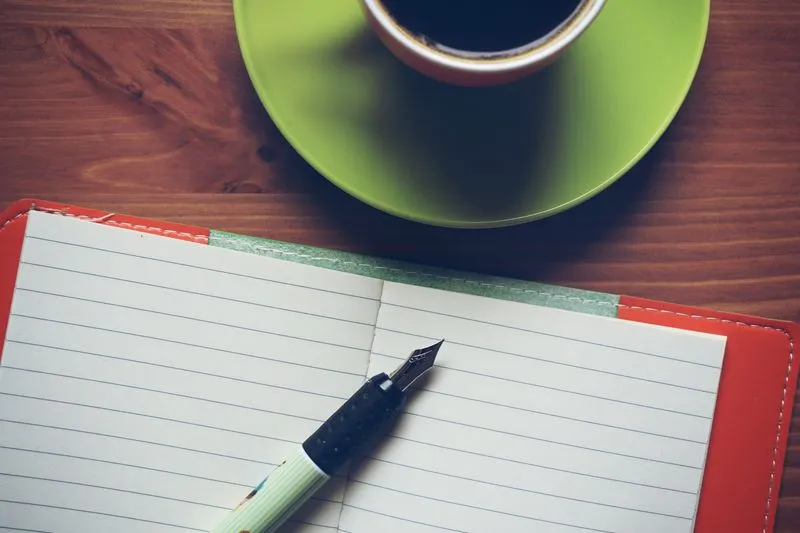 Agenda papier ouvert sur un bureau, à côté d'un stylo et d'une tasse