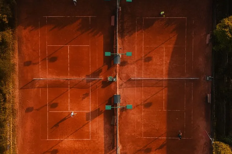 Deux courts de tennis en terre battue orange vus d'en haut, avec des joueurs qui s'entraînent