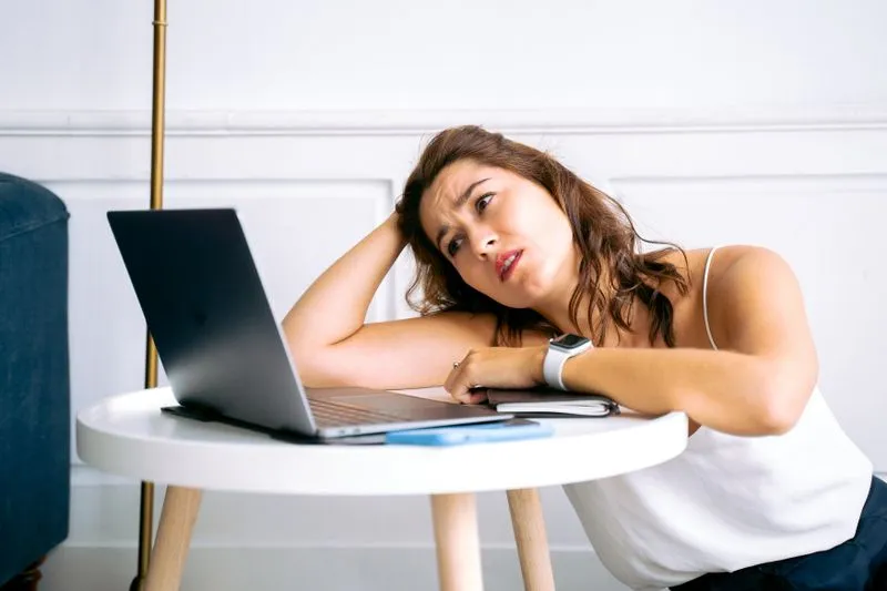 Jeune femme assise devant un ordinateur portable, le menton dans la main, qui attend devant l'écran