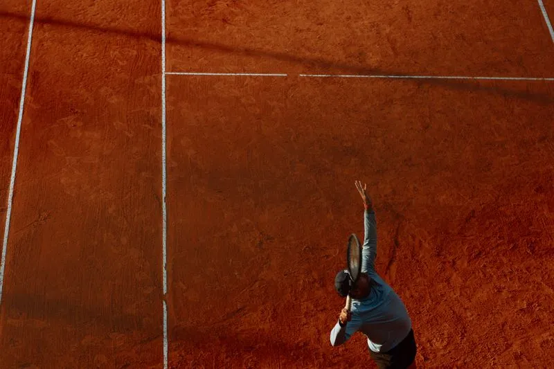Joueur de tennis vu d'en haut qui sert sur un court de terre battue orange