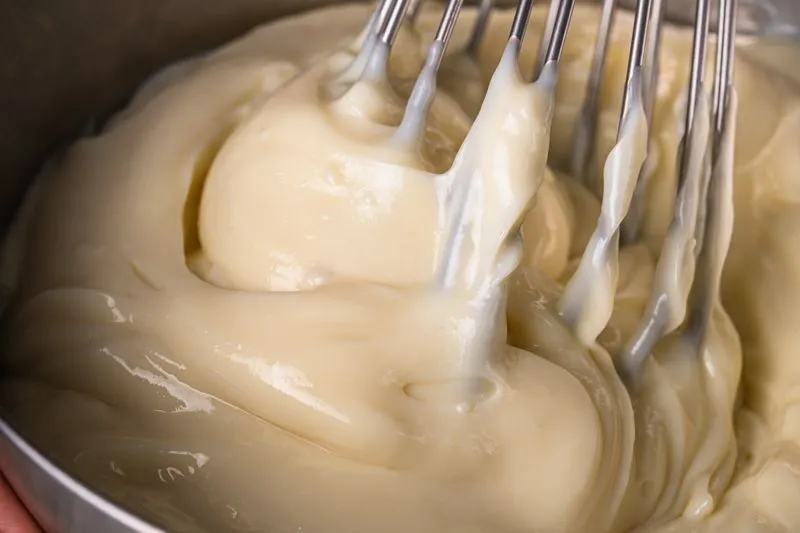 Crème pâtissière épaisse et lisse, travaillée au fouet dans un cul-de-poule en inox
