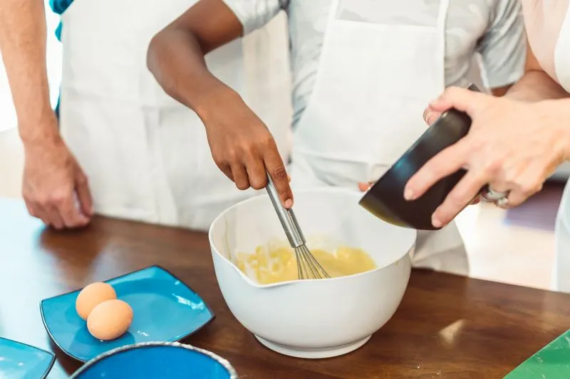 Mains fouettant des œufs et du sucre dans un saladier blanc, lors d'un atelier de cuisine