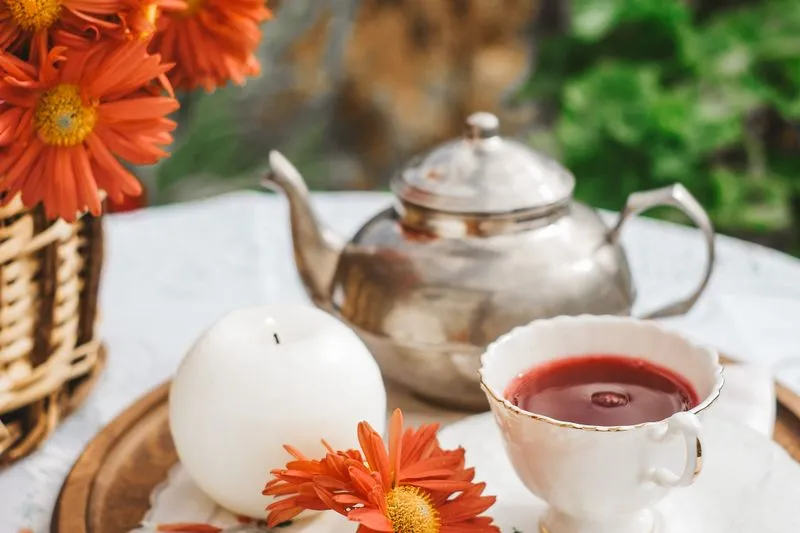 Théière, tasse de thé rouge et bouquet de fleurs orange sur une table de jardin