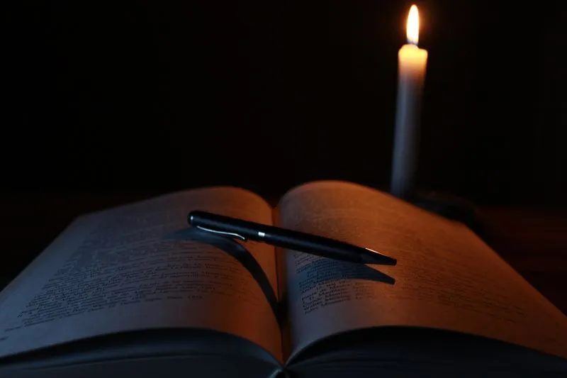 Carnet ouvert et stylo posés sur une table en bois, à côté d'une bougie allumée, le soir