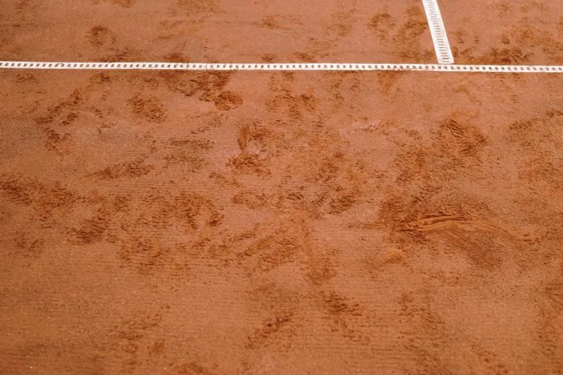 Gros plan sur la terre battue ocre d'un court de tennis, traversée par une ligne blanche