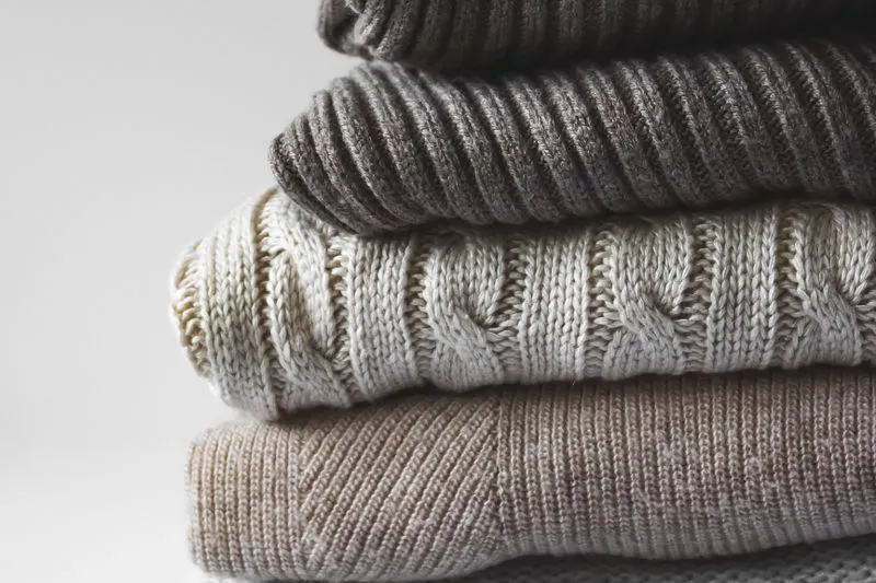 Pull en maille torsadée écrue, plié dans une pile de pulls en laine