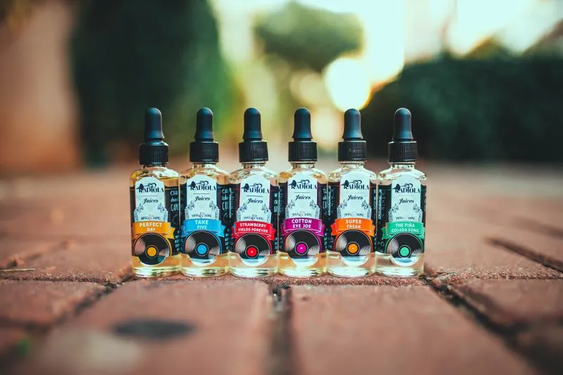Six flacons d'e-liquide aux étiquettes colorées, alignés en extérieur