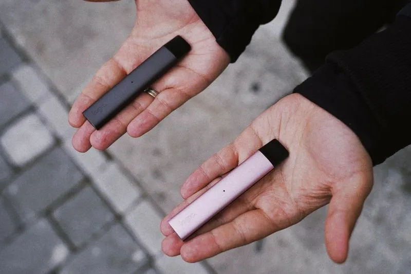 Deux cigarettes électroniques, grise et rose, posées dans le creux de deux mains