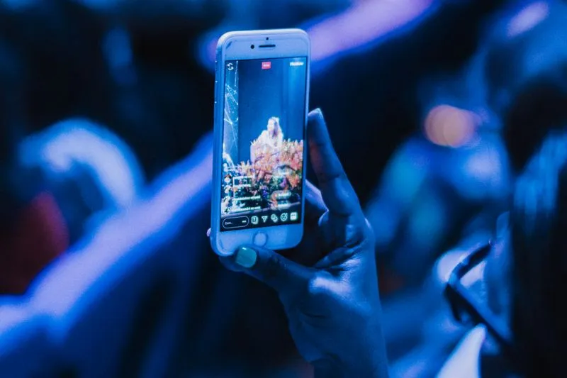 Main tenant un smartphone qui filme une scène de concert, éclairage bleu et foule floue en arrière-plan