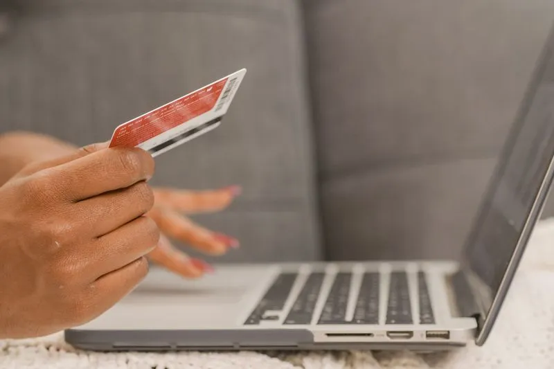 Main tenant une carte bancaire à côté du clavier d'un ordinateur portable, pendant un paiement en ligne