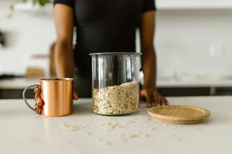 Bocal en verre rempli de flocons d'avoine, à côté d'une tasse en cuivre