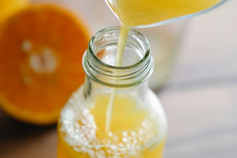 Jus d'orange fraîchement pressé versé dans une bouteille en verre, à côté d'une orange coupée en deux