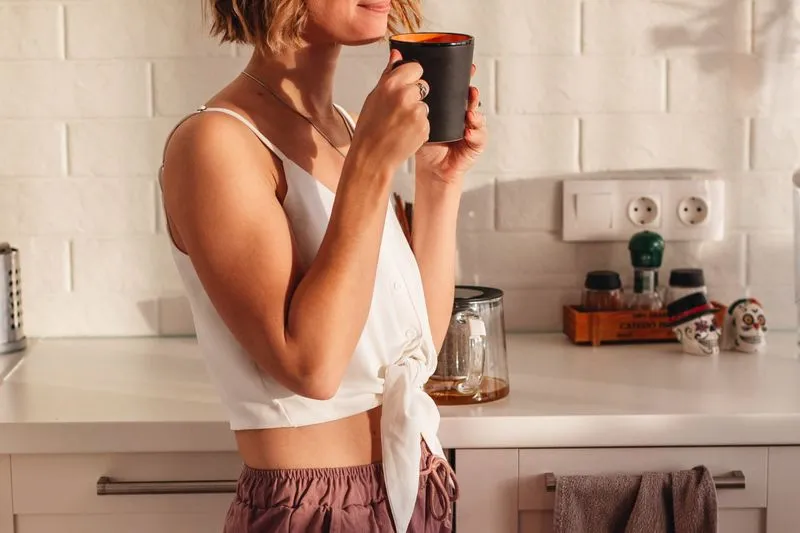Jeune femme buvant un café dans une cuisine baignée de lumière du matin
