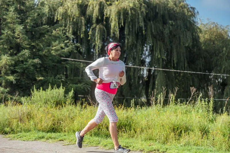 Femme qui court seule sur un chemin bordé de verdure, dossard de course à la taille
