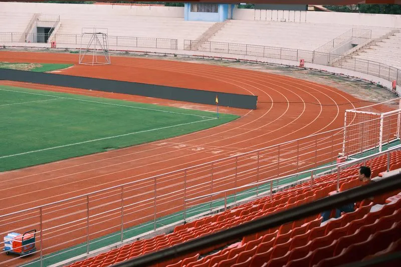 Piste d'athlétisme rouge autour d'une pelouse de football, vue depuis des tribunes presque vides