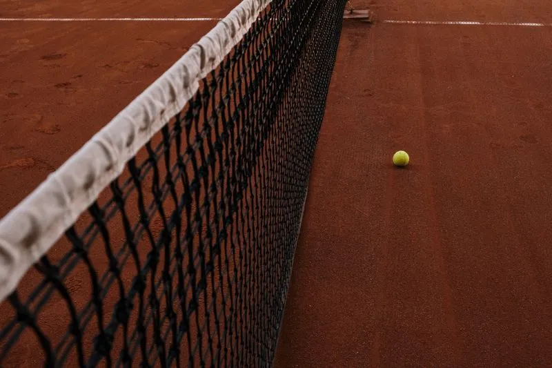 Filet et balle de tennis sur un court en terre battue ocre, lignes blanches visibles