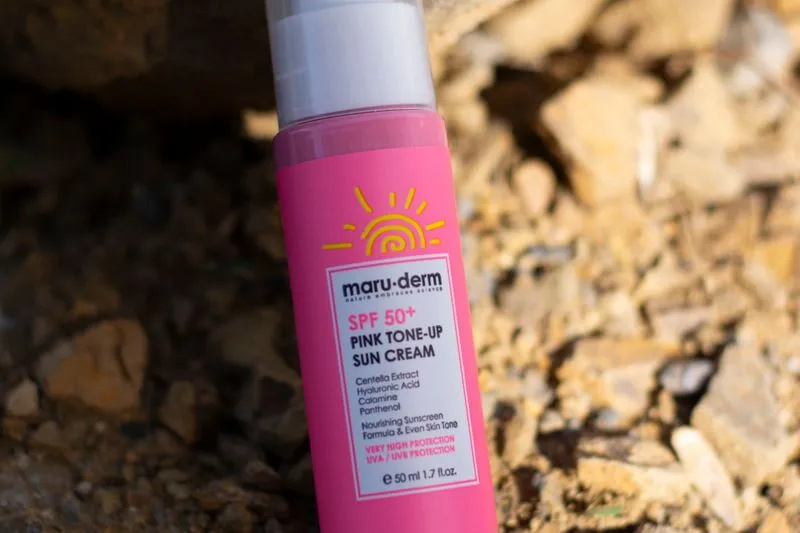 Gros plan sur un tube de crème solaire rose, avec son SPF et ses ingrédients actifs affichés sur l'étiquette