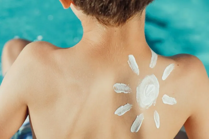 Soleil dessiné à la crème solaire blanche sur le dos d'un enfant, devant une eau turquoise