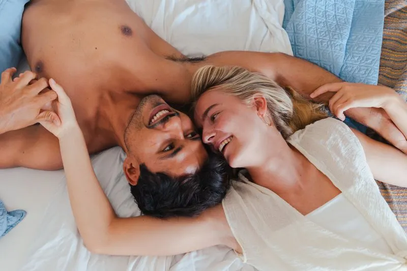 Couple allongé tête contre tête sur un lit, riant en se tenant la main