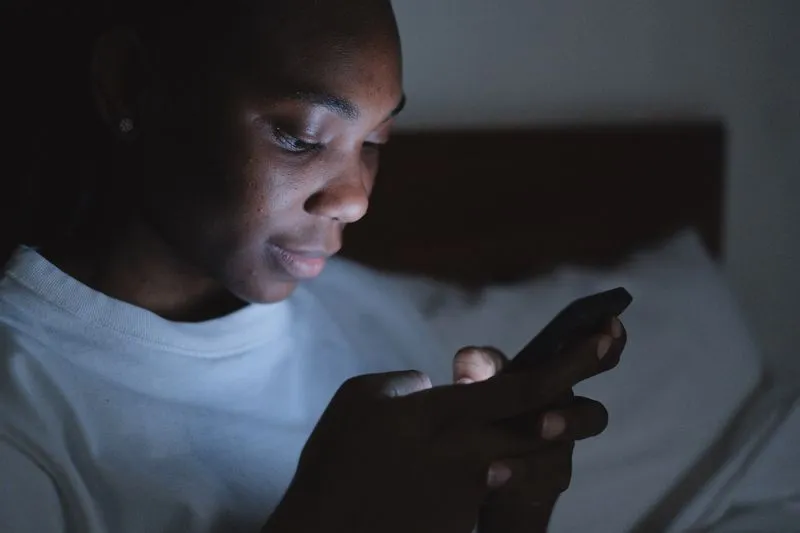 Jeune femme éclairée par l'écran de son téléphone, dans la pénombre d'une chambre