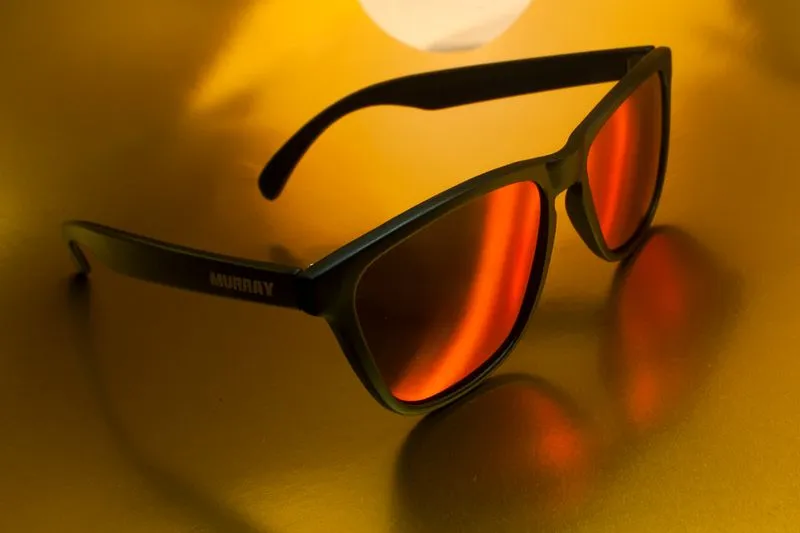 Gros plan sur la branche d'une paire de lunettes de soleil à verres miroir orange, avec un nom imprimé dessus