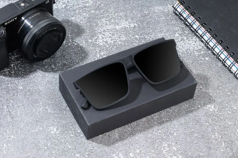 Lunettes de soleil noires posées sur leur étui ouvert, à côté d'un appareil photo, sur une surface en pierre