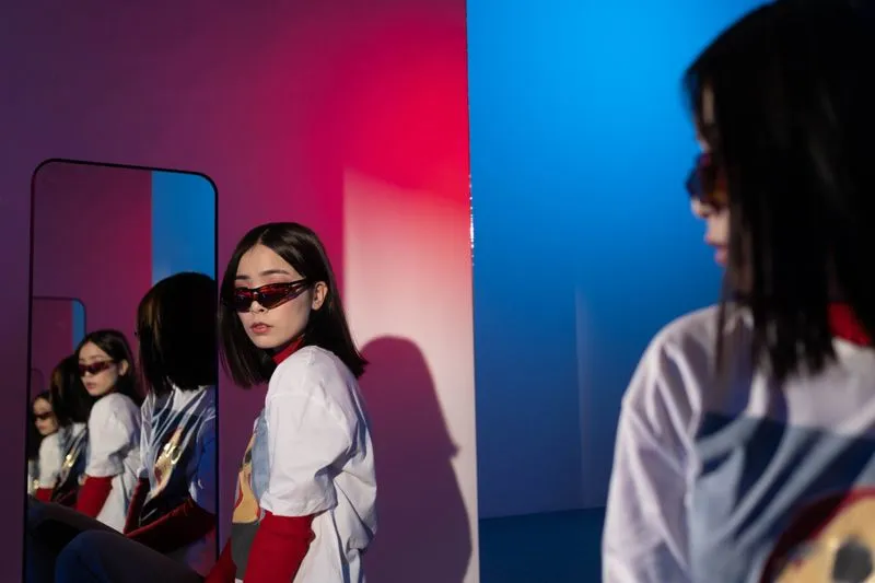 Femme en petites lunettes de soleil teintées rouge, debout devant un miroir, éclairage rouge et bleu