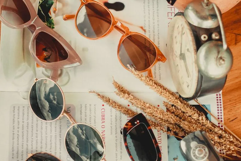 Assortiment de lunettes de soleil aux formes variées — œil-de-chat rose, rondes ambrées, rondes dorées et rectangulaires écaille — posées sur un magazine