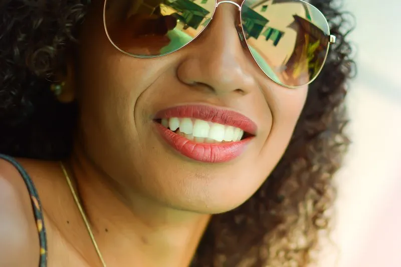 Femme souriante en lunettes de soleil aviateur à verres miroir, gros plan en plein soleil de début d'été